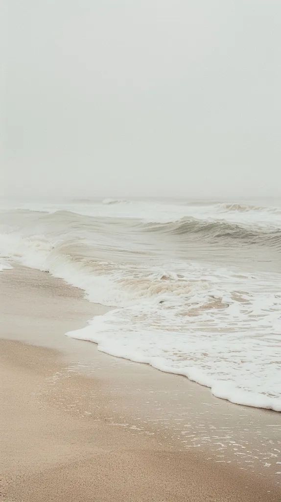 an empty beach with waves coming in to shore and one person walking on the sand