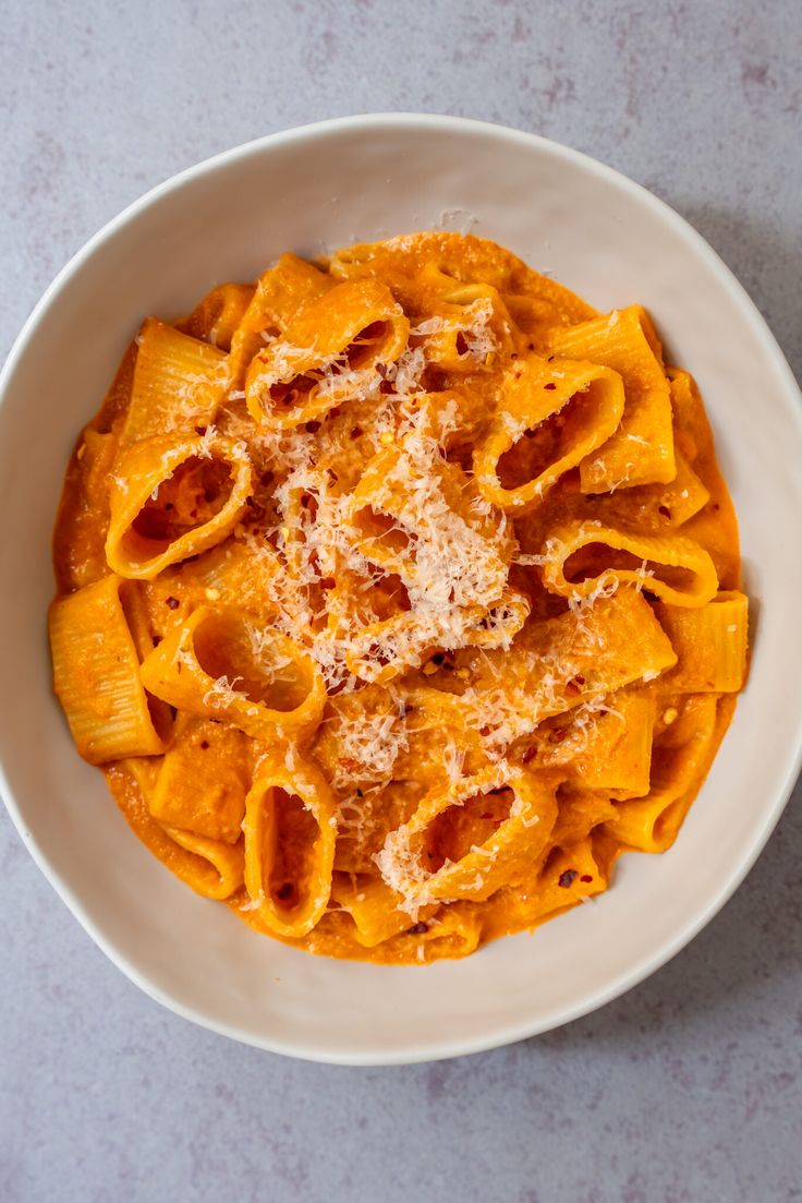 a white bowl filled with pasta and sauce on top of a gray countertop next to a fork