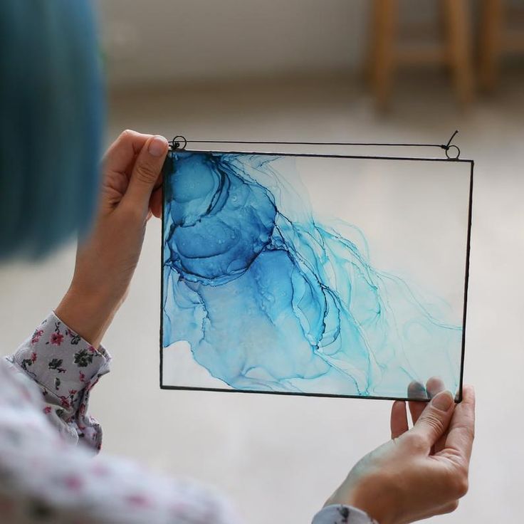 a woman holding up a piece of art that looks like blue fluid paint on glass