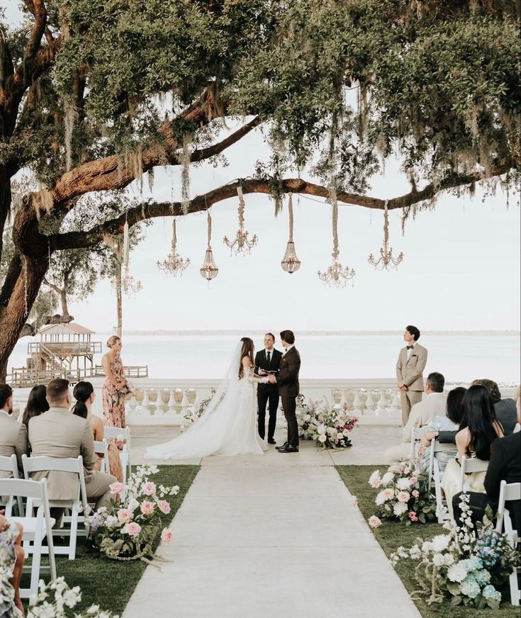 a bride and groom are standing under the trees at their wedding ceremony on the beach