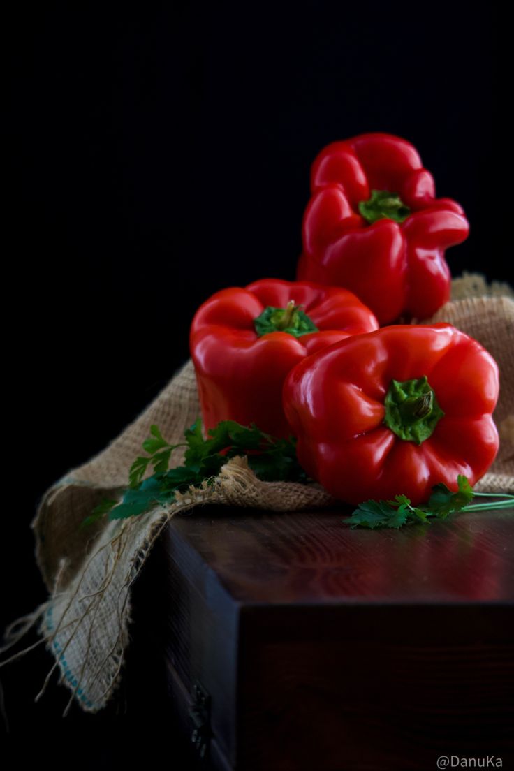 three red bell peppers sitting on top of a wooden table next to burlocks