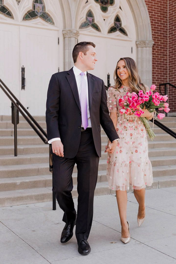 a man and woman are walking down the street holding flowers in their hands as they walk towards an old church