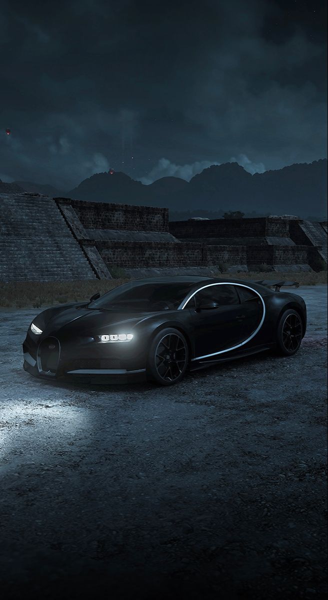 a bugatti car parked in front of an ancient structure at night with the lights on