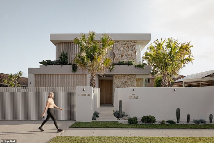 a woman walking down the street in front of a house with palm trees on it