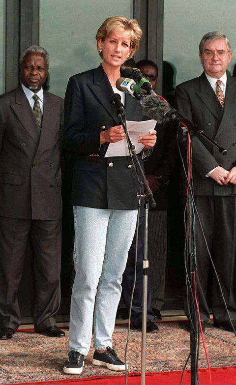 a woman standing at a podium with microphones in front of her and other people behind her