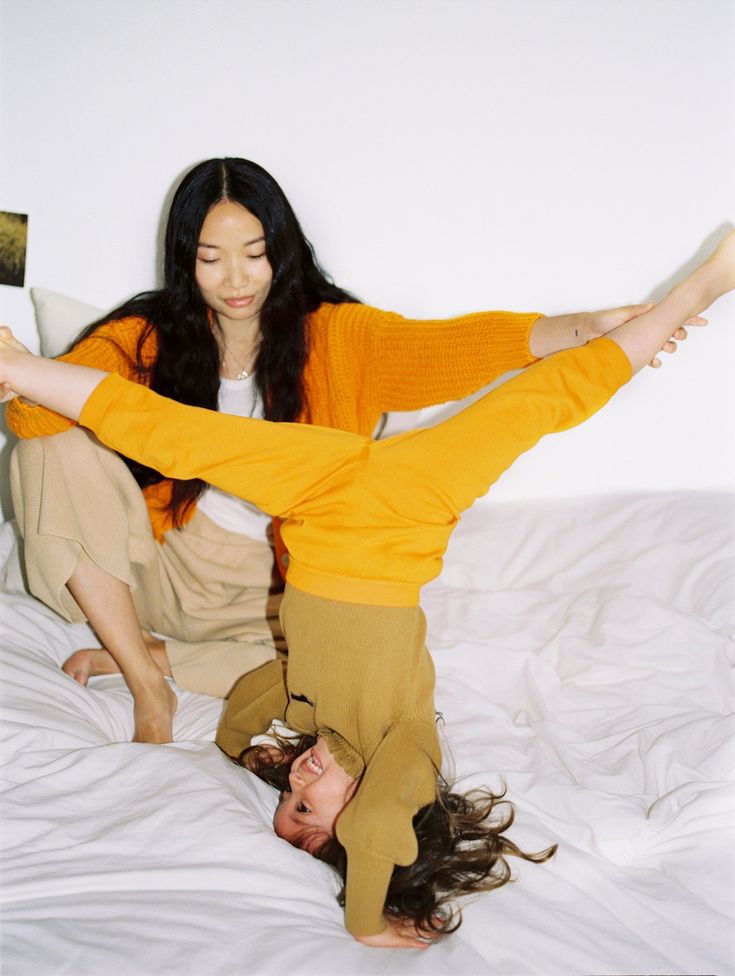 two women are laying on the bed and one is holding her leg in the air