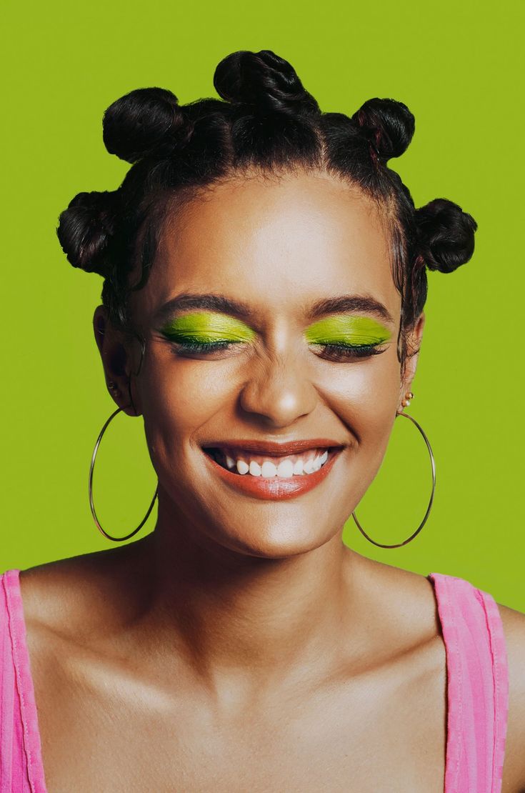 a woman with bright green eyeshades and large hoop earrings smiles at the camera