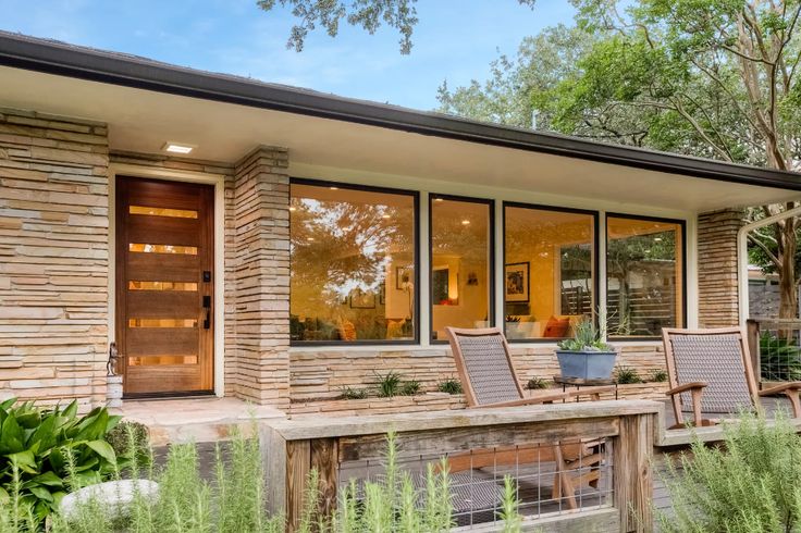 a modern home with large windows and wooden furniture in the front porch area, surrounded by greenery