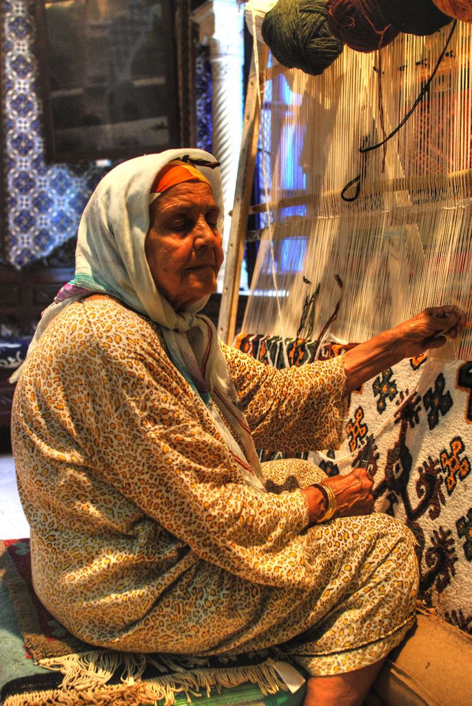 an old woman sitting in front of a weaving machine with yarn on it's sides