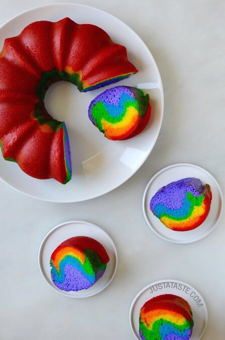 a rainbow bundt cake on a plate next to two small white bowls with one piece cut out