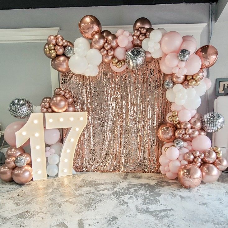 a table topped with balloons and a giant number 17 balloon arch filled with pink, white and gold balloons