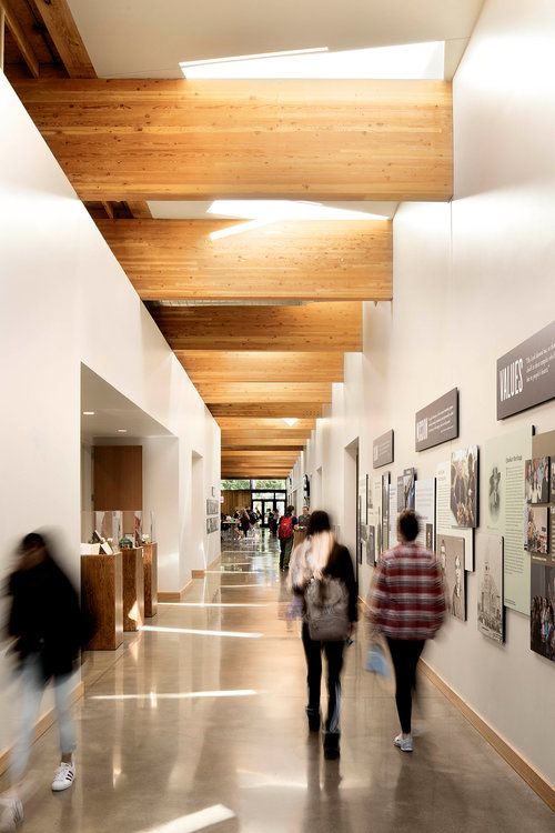 two people walking down a long hallway with pictures on the walls and wood ceilinging