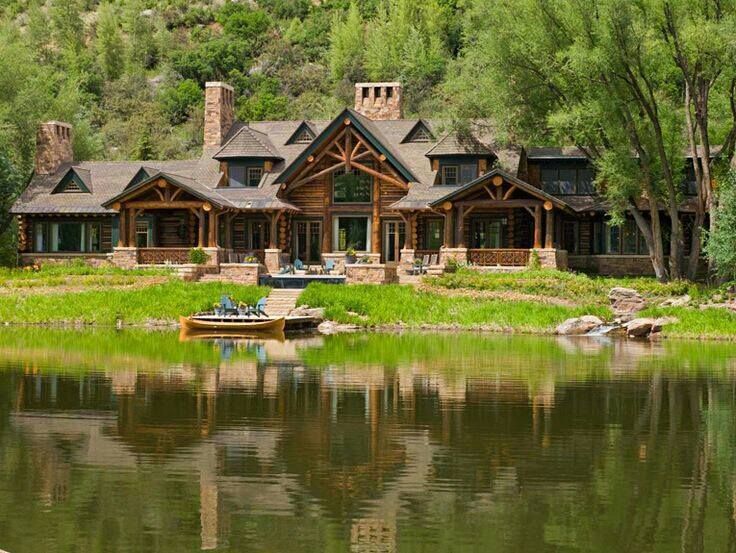 a large house sitting on top of a lush green hillside next to a lake in front of a forest