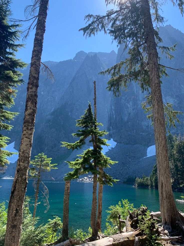 the sun shines through the trees in front of a mountain lake and some mountains