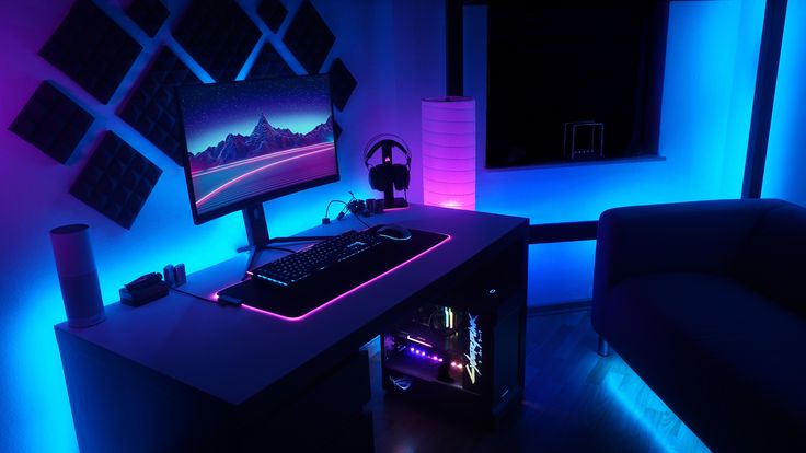 a computer desk with a keyboard, mouse and monitor lit up by blue lights in the room