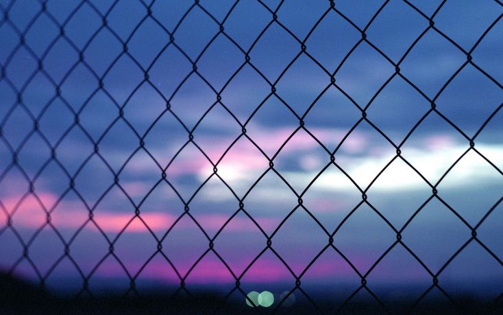 the sky is purple and blue as seen through a chain link fence