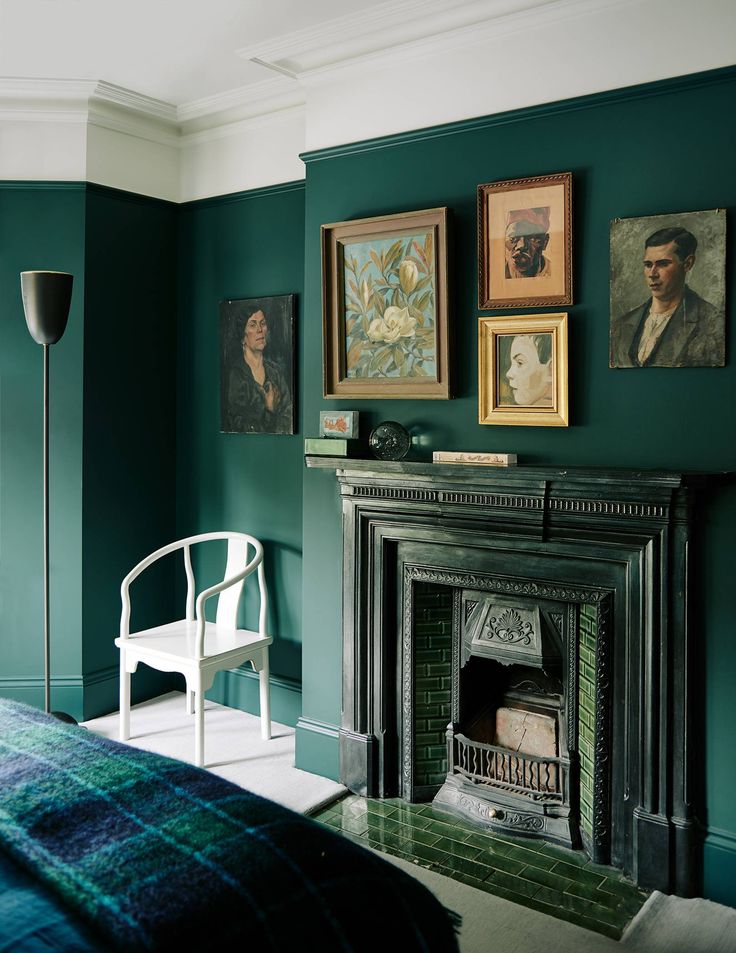 a bedroom with green walls and pictures on the wall above the fireplace, along with a white chair