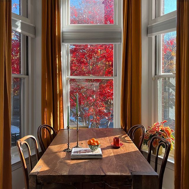 a wooden table sitting in front of two windows with red leaves on the trees outside