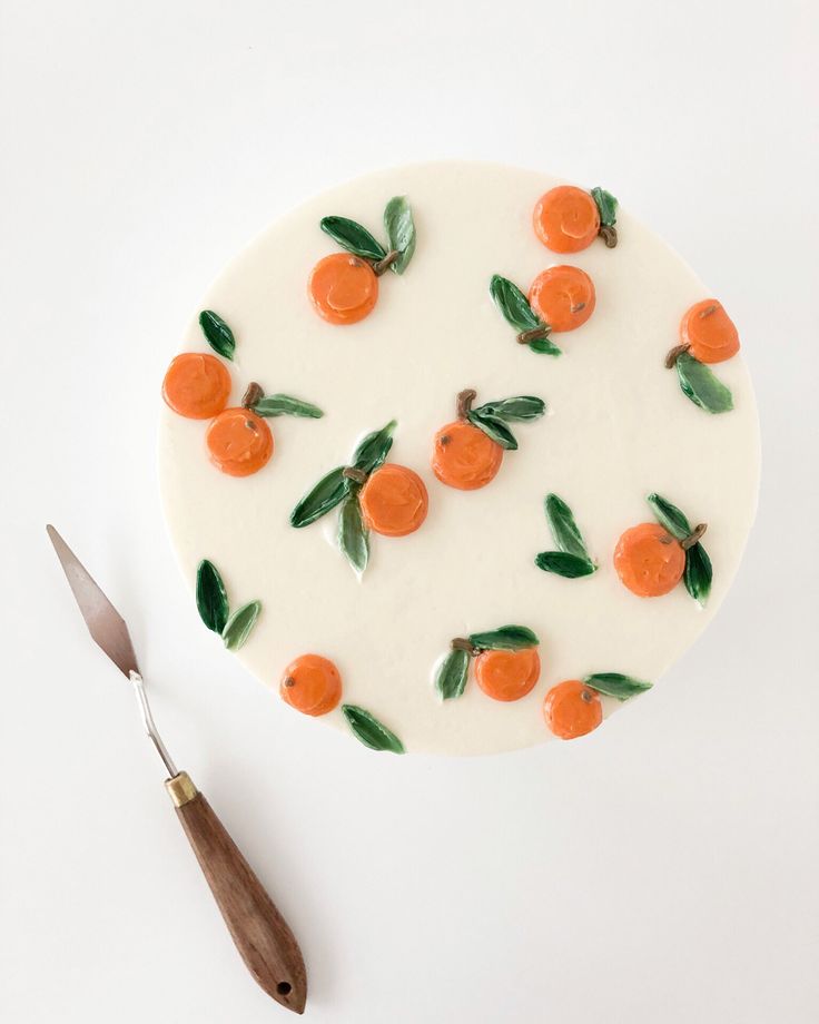 a cake decorated with oranges and leaves on top of a white plate next to a knife