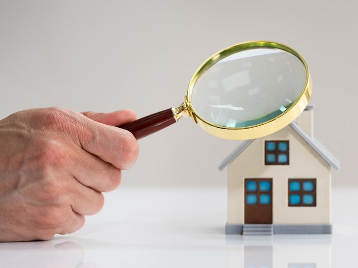 a hand holding a magnifying glass over a house