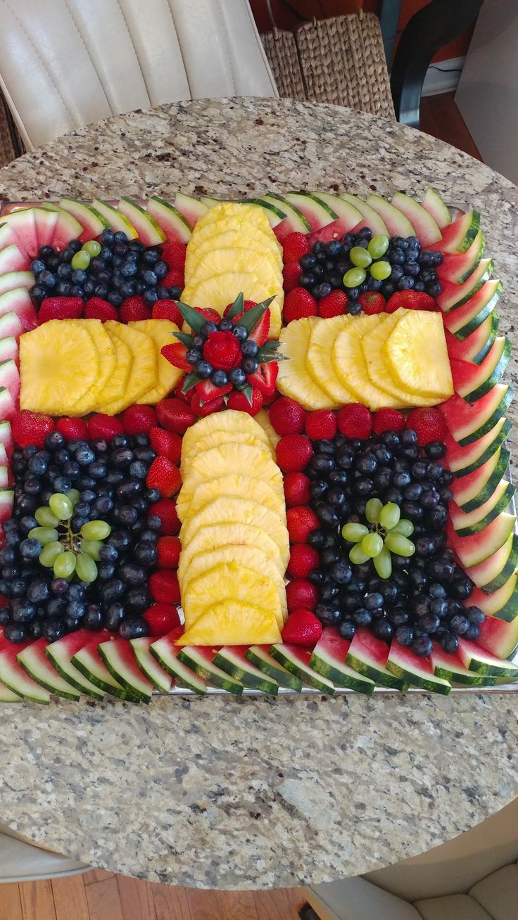 a cake decorated with fruits and vegetables on a table top, in the shape of a cross