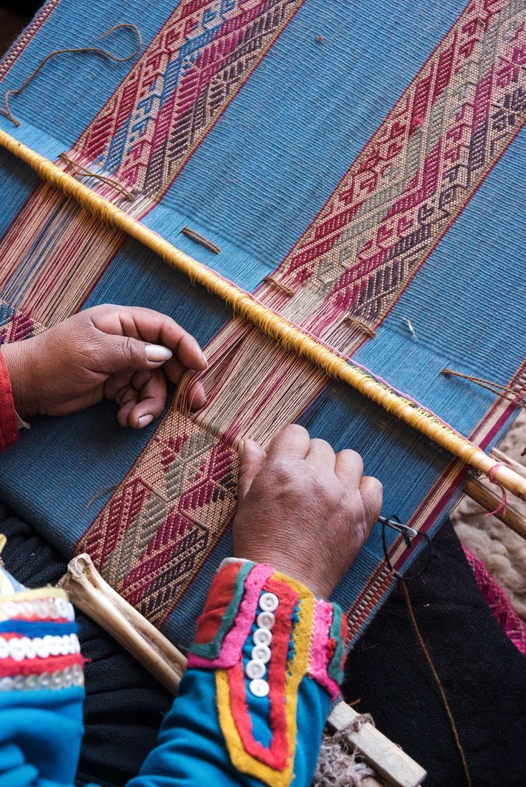 a person is weaving something on a large piece of cloth with a wooden pole in the background