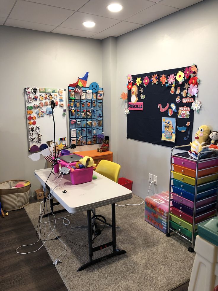 a room with several tables, chairs and toys on the floor in front of a chalkboard