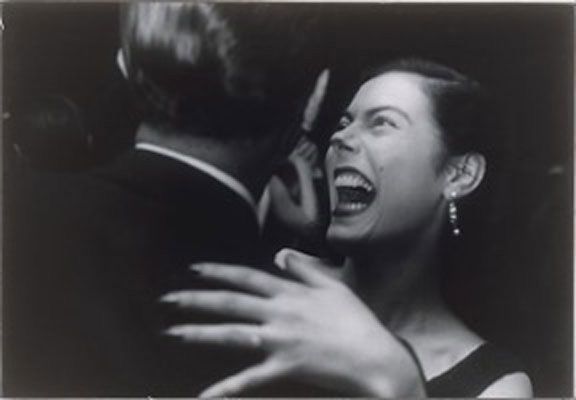 a black and white photo of a woman laughing with her hands on the back of another woman's shoulder