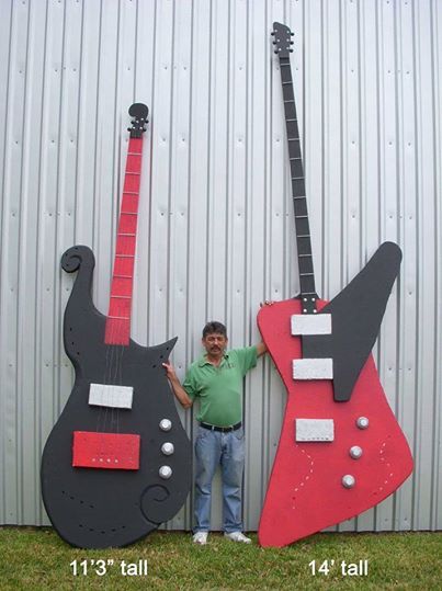 a man standing next to two guitars made out of paper mache, one is red and the other is black