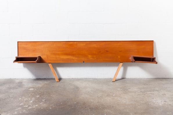 a wooden bench sitting on top of a cement floor next to a white brick wall