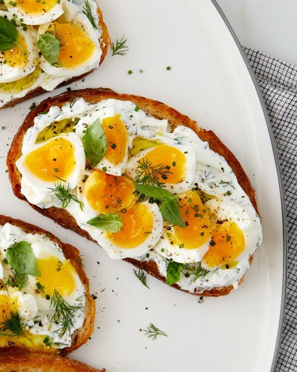 three pieces of toast with eggs and herbs on them, sitting on a white plate