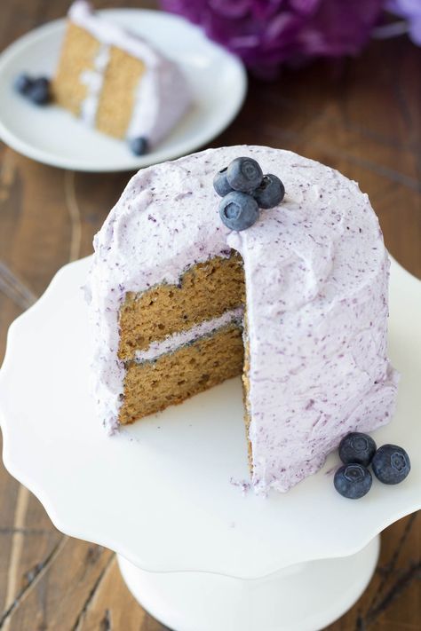 a cake with white frosting and blueberries is on a plate next to purple flowers