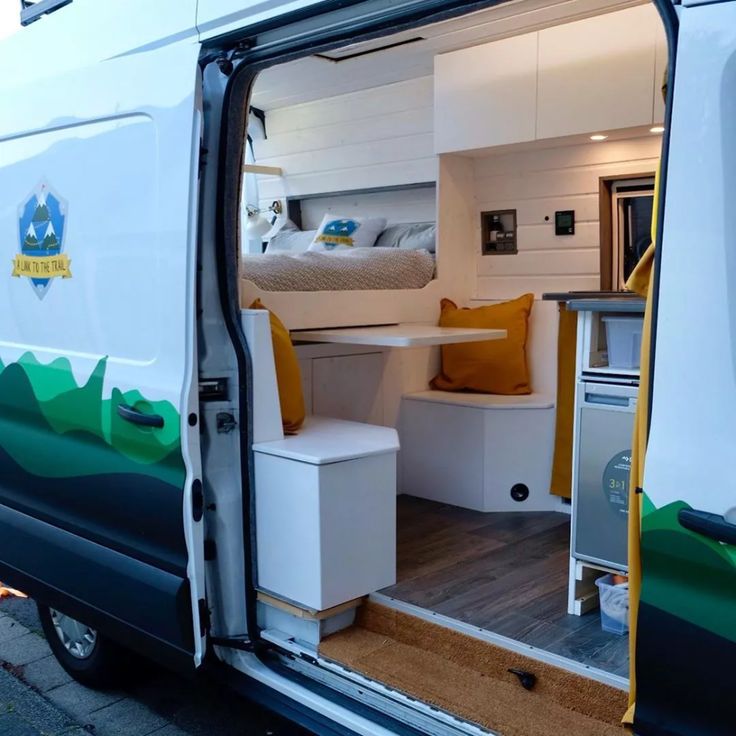 the interior of a camper van with its door open to reveal a bed and kitchen