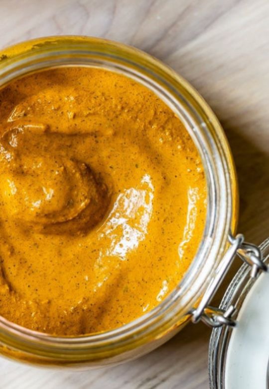 a glass jar filled with mustard sitting on top of a wooden table next to a spoon