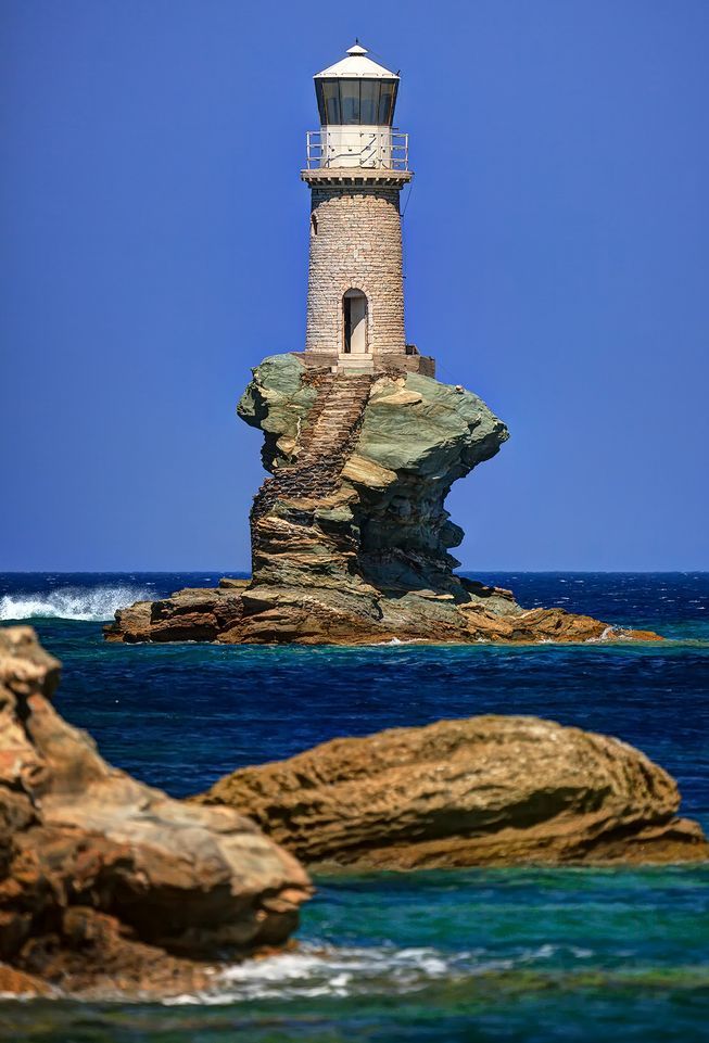 a light house sitting on top of a rocky cliff near the ocean under a blue sky