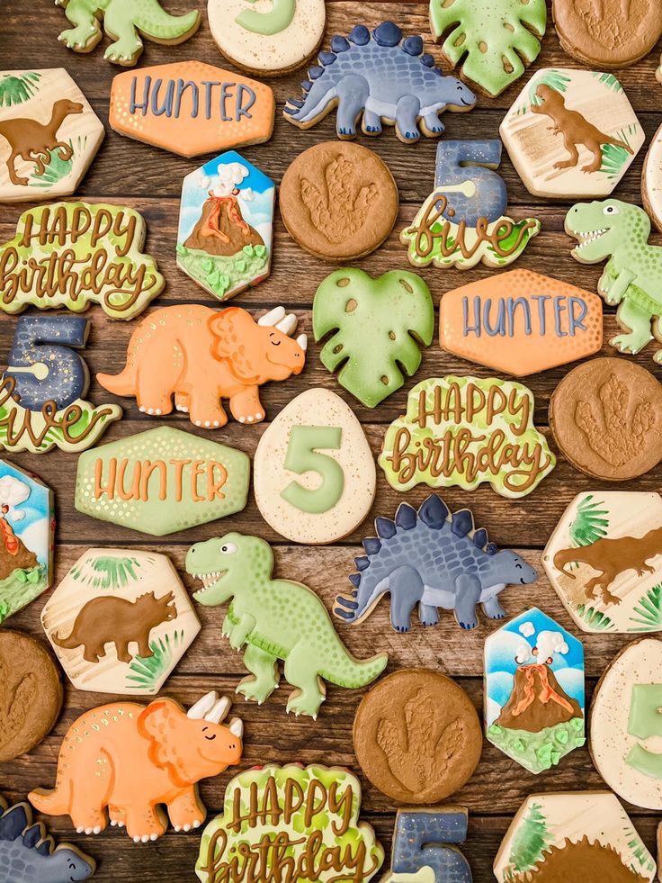 dinosaur birthday cookies are arranged on a wooden table with the numbers 5, 6, and 7