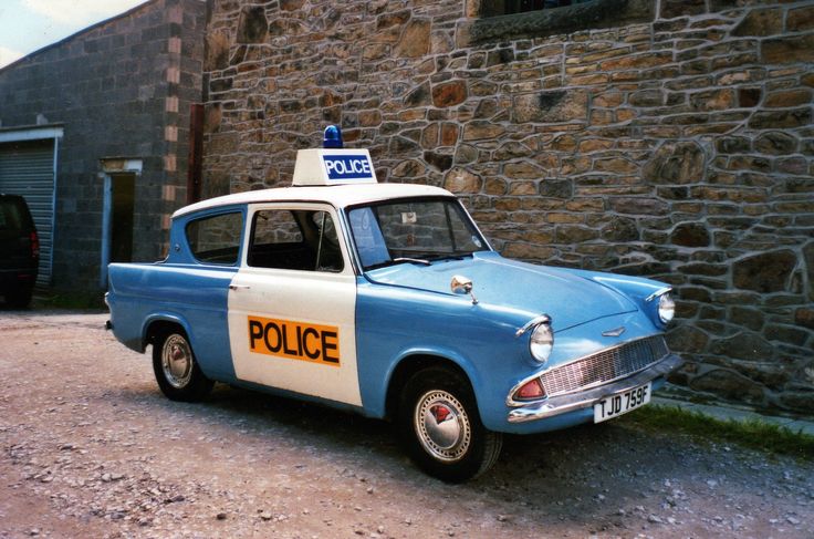 an old police car parked in front of a stone building with a sign on top