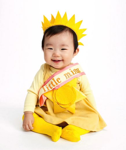 a baby sitting on the ground wearing a yellow sun costume and smiling at the camera