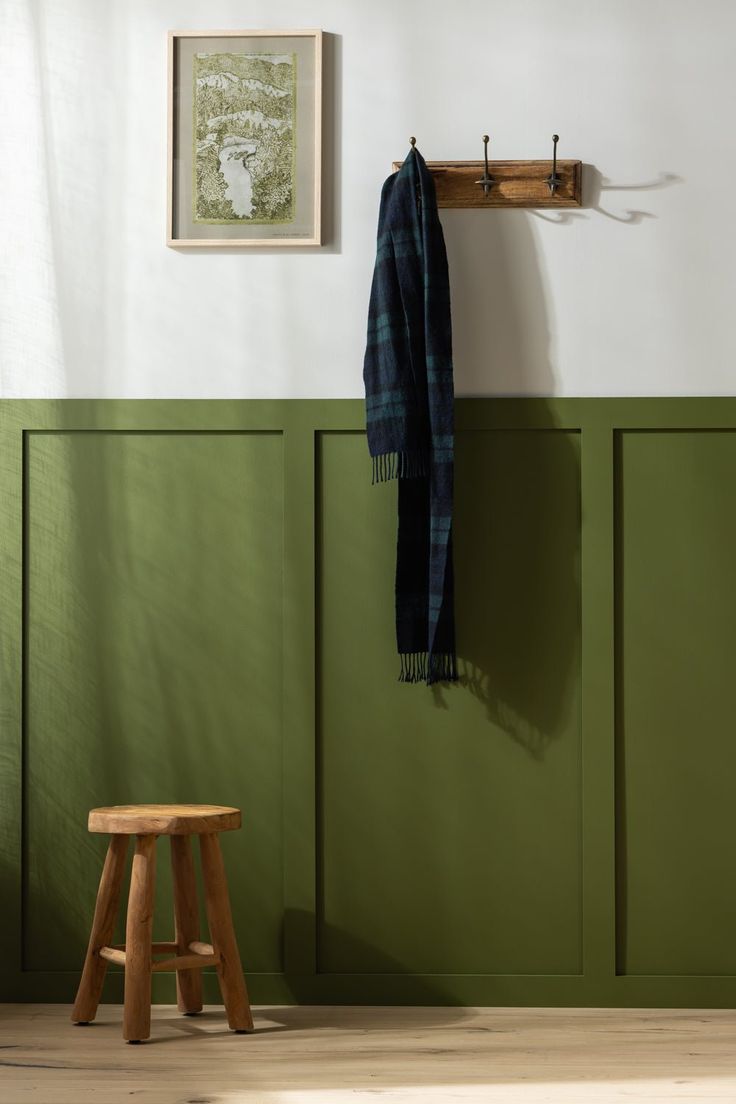 a wooden stool sitting next to a green wall with a scarf hanging on it's hook