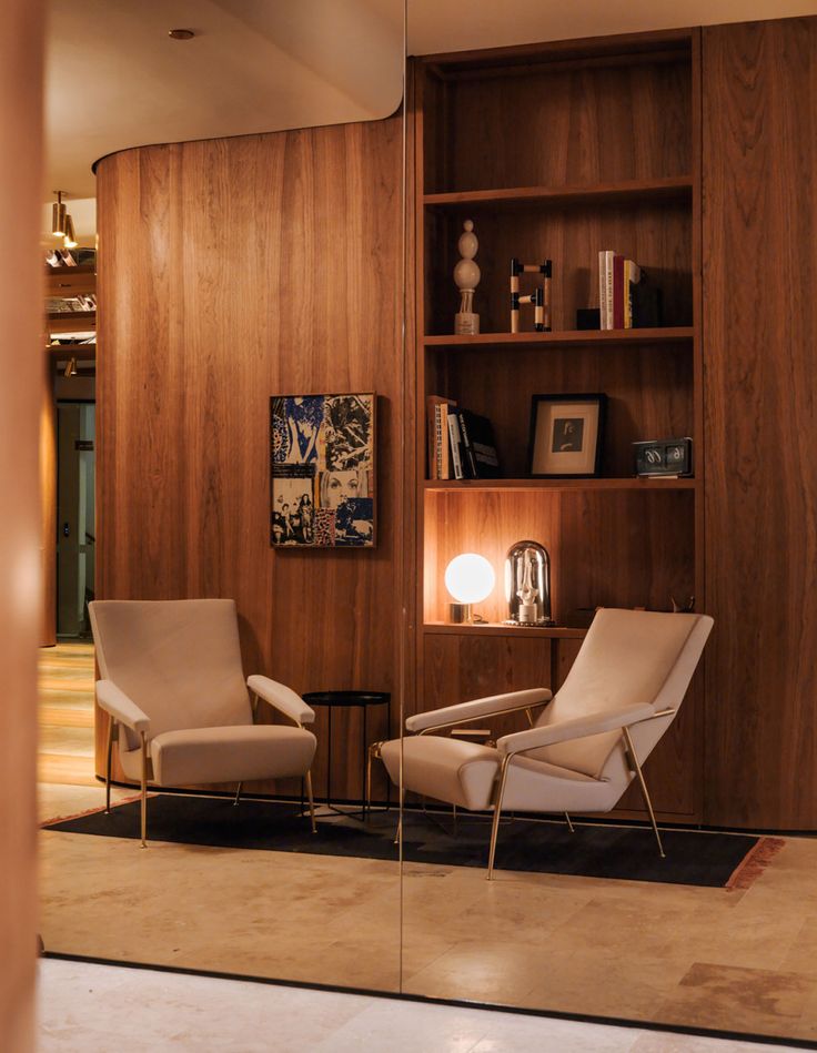 a living room with two chairs and a book shelf on the wall next to it