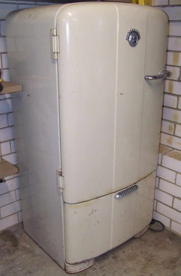 an old white refrigerator sitting inside of a room next to a brick wall and shelves