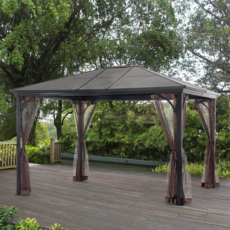 a gazebo on a deck in the middle of a garden with trees and bushes