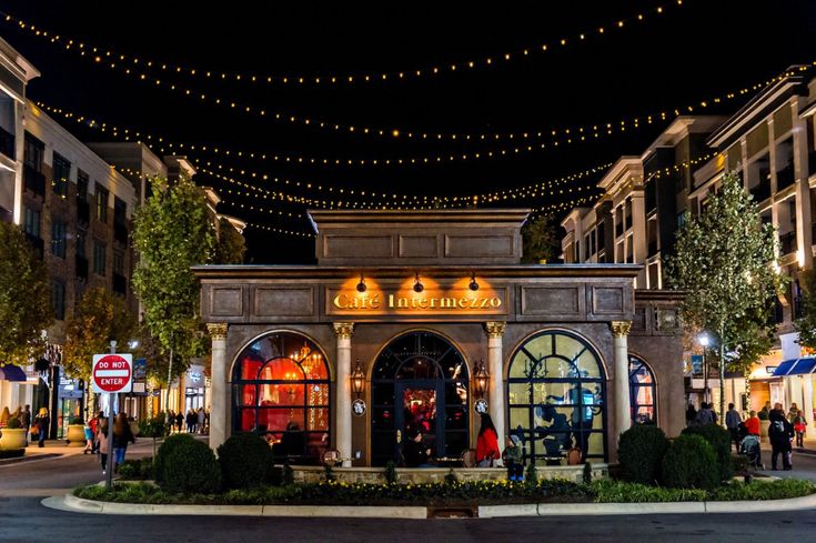 people are walking around in front of a store at night with lights strung over the building