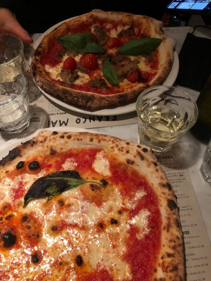 two pizzas sitting on top of a table next to glasses