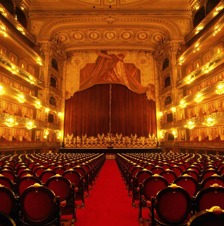 an empty auditorium with red carpet and gold decorations on the walls, along with rows of chairs