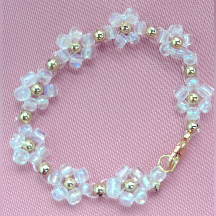 a bracelet with glass beads and gold accents on a pink background, the bead is attached to an adjustable clasp