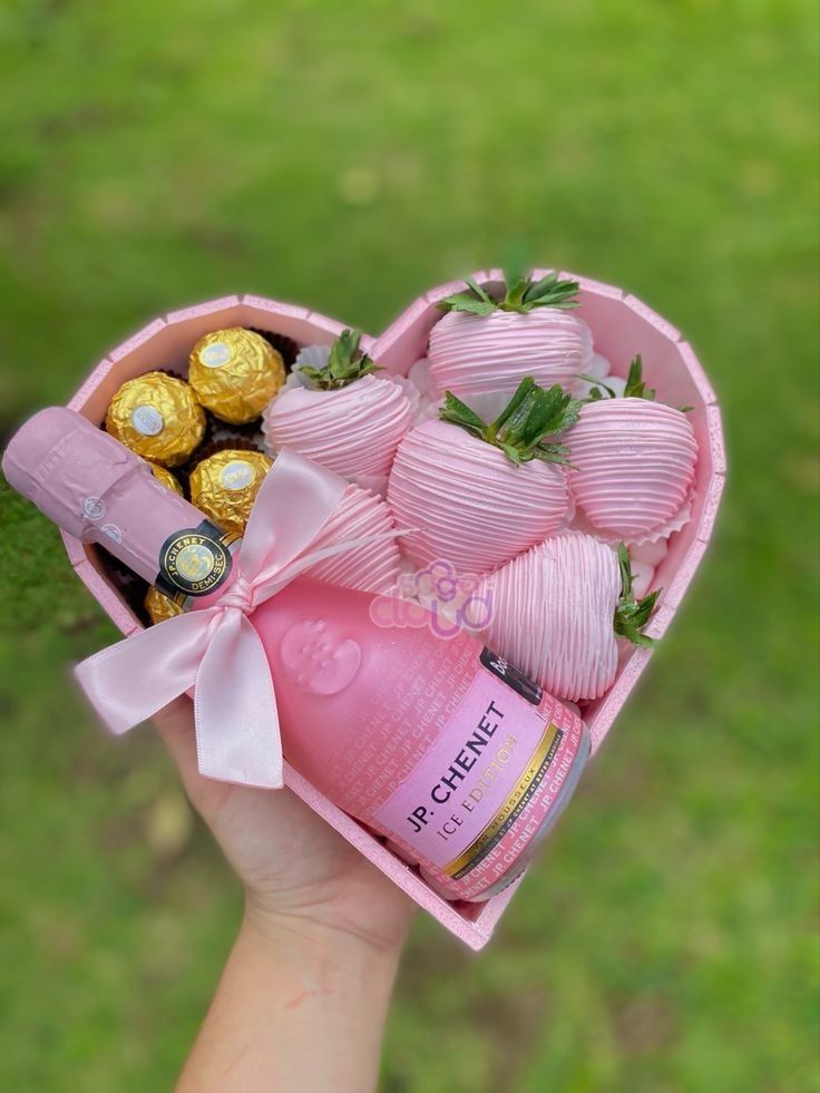 a pink heart shaped box filled with chocolates and strawberries in someone's hand