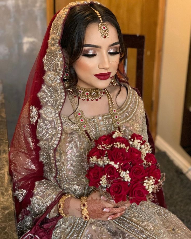 a woman in a red and gold bridal outfit holding a bouquet of flowers on her wedding day