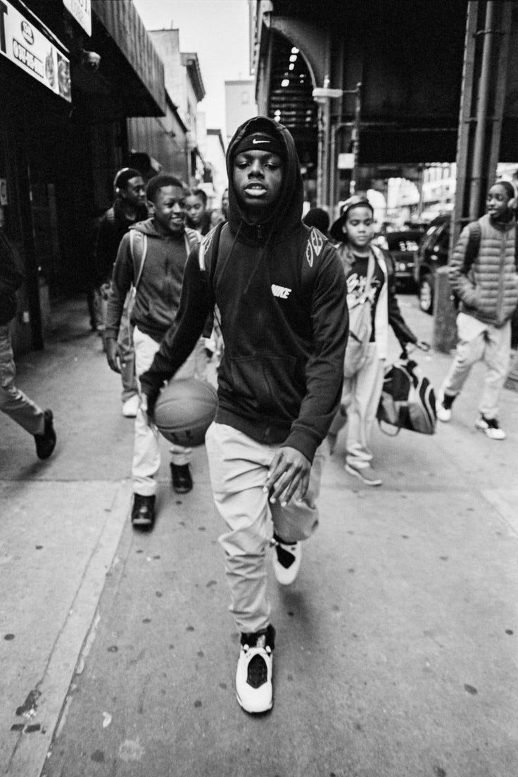 a black and white photo of a man holding a basketball on the street with other people walking by