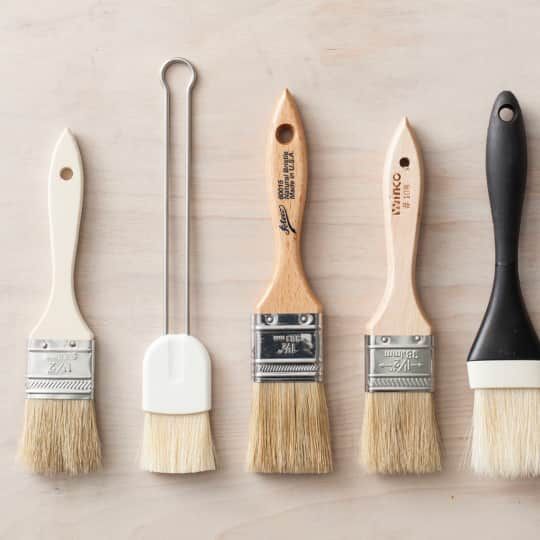 four paint brushes lined up in a row on top of a wooden table next to each other